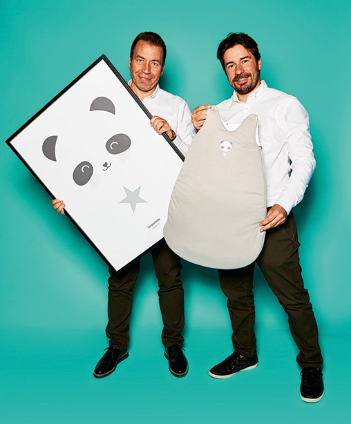 Javier Vivas und Oscar Vivas, Inhaber von bonjourbébé Premium, mit Schlafsack und Poster der "Panda Collection"